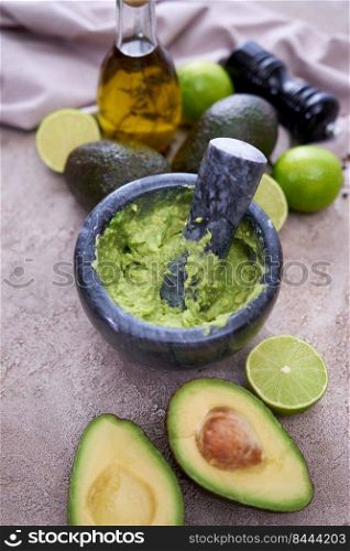 making guacamole - crushed avocado in marble mortar on grey concrete table.. making guacamole - crushed avocado in marble mortar on grey concrete table