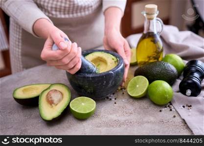 making guacamole - woman holding pestle to crush avocado in marble mortar on grey concrete table.. making guacamole - woman holding pestle to crush avocado in marble mortar on grey concrete table