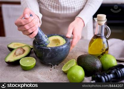 making guacamole - woman holding pestle to crush avocado in marble mortar on grey concrete table.. making guacamole - woman holding pestle to crush avocado in marble mortar on grey concrete table