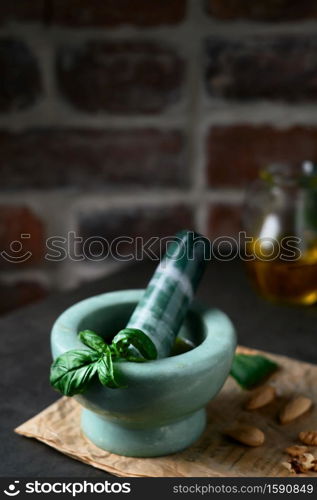 Making homemade pesto sauce in a marble mortar. Focus on basil leaves in a mortar. Kitchen, olive oil, nuts, basil and spices on a wooden table, close-up.