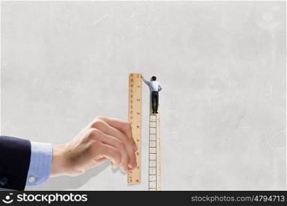 Making measures. Businessman standing on ladder and hand with wooden ruler