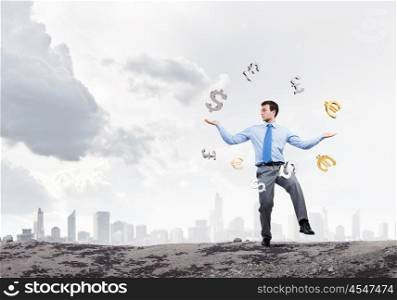 Making money. Young businessman juggling with currency symbols against city background
