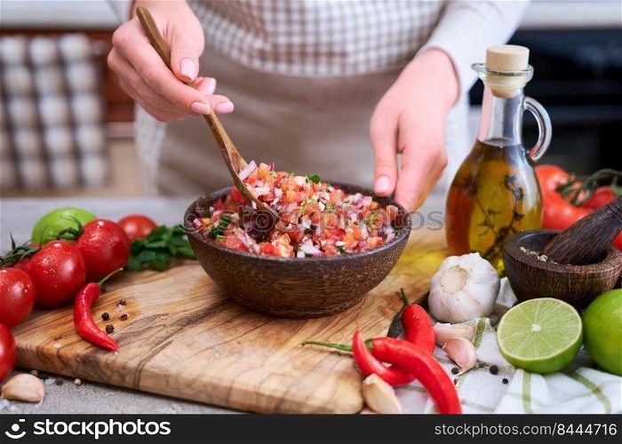 making salsa dip sauce - woman mixing chopped ingredients in wooden bowl.. making salsa dip sauce - woman mixing chopped ingredients in wooden bowl