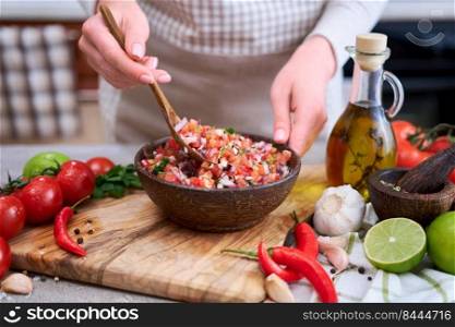 making salsa dip sauce - woman mixing chopped ingredients in wooden bowl.. making salsa dip sauce - woman mixing chopped ingredients in wooden bowl