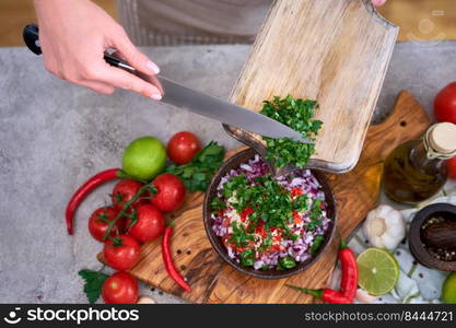 making salsa dip sauce - woman pouring chopped cilantro or parsley to wooden bowl.. making salsa dip sauce - woman pouring chopped cilantro or parsley to wooden bowl