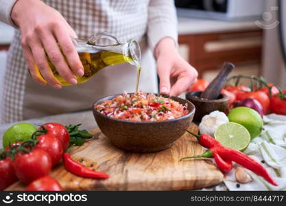 making salsa dip sauce - woman pouring olive oil to wooden bowl with chopped ingredients.. making salsa dip sauce - woman pouring olive oil to wooden bowl with chopped ingredients