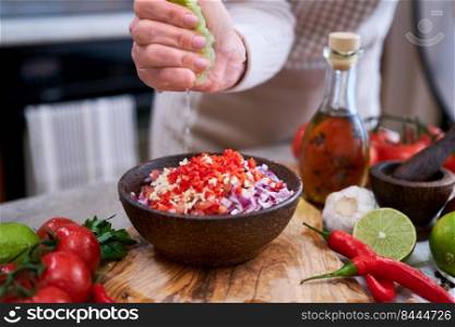 making salsa dip sauce - woman squeezing fresh lime juice to chopped ingredients in wooden bowl.. making salsa dip sauce - woman squeezing fresh lime juice to chopped ingredients in wooden bowl