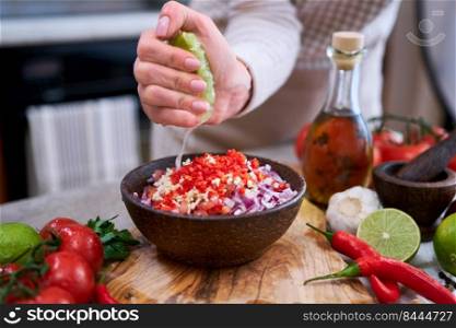 making salsa dip sauce - woman squeezing fresh lime juice to chopped ingredients in wooden bowl.. making salsa dip sauce - woman squeezing fresh lime juice to chopped ingredients in wooden bowl