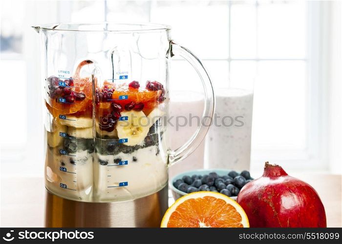 Making smoothies in blender with fruit and yogurt. Prepared smoothies and healthy smoothie ingredients in blender with fresh fruit ready to blend on kitchen table