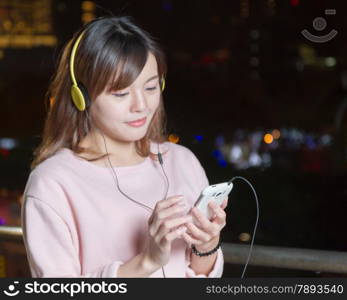 Malaysian female wearing yellow headphones and holding cell phone with city lights in background