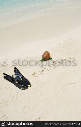 Maldives written in a sandy beach with coconut and snorkeling equipment