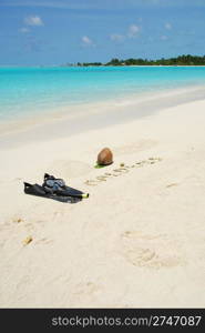 Maldives written in a sandy beach with coconut and snorkeling equipment