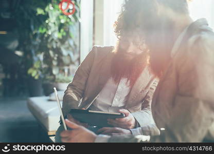 Male adult hipster twins working on digital tablet and laptop in office