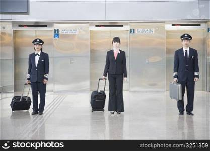 Male and a female pilot standing with a female cabin crew in front of elevators