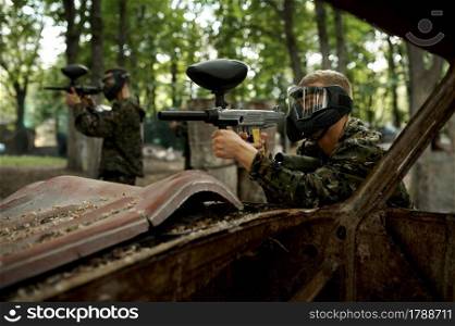 Male and famale warriors in camouflages and masks aimimg with paintball guns. Extreme sport with pneumatic weapon and paint bullets or markers, military team game outdoors. Warriors aimimg with paintball guns, team game