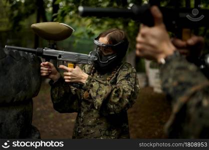 Male and famale warriors in camouflages and masks aimimg with paintball guns. Extreme sport with pneumatic weapon and paint bullets or markers, military team game outdoors, combat tactics. Warriors aimimg with paintball guns, team game