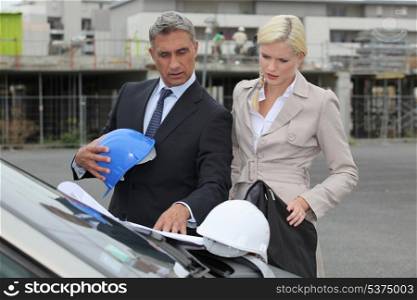 Male and female architects stood by car