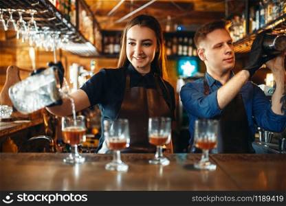 Male and female bartender at the bar counter. Alcohol drink preparation. Two barmans working in pub. Male and female bartender at the bar counter