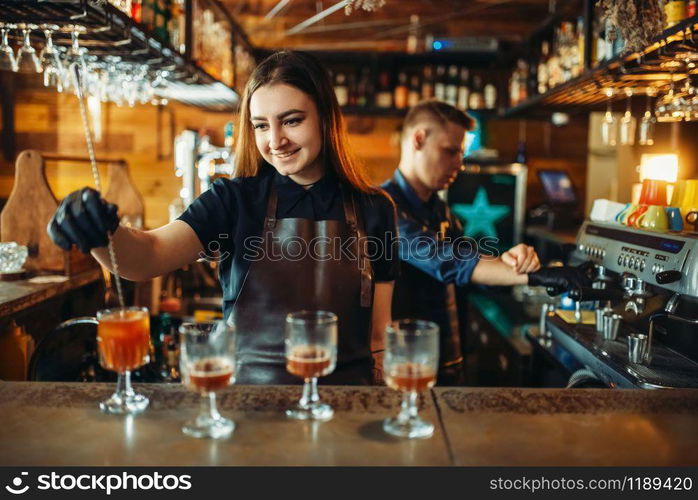 Male and female bartender at the bar counter. Alcohol drink preparation. Two barmans working in pub. Male and female bartender at the bar counter