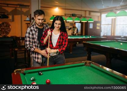 Male and female billiard players with cue at the table with colorful balls. Man and woman plays pool game in sport bar. Male and female billiard players with cue