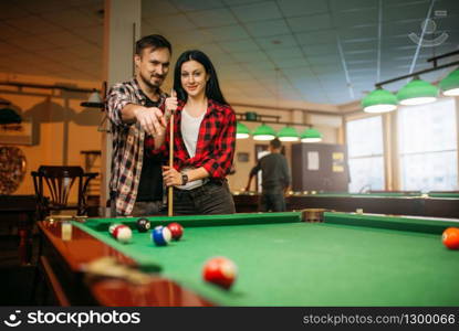 Male and female billiard players with cue at the table with colorful balls. Man and woman plays american pool game in sport bar