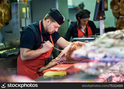 Male and female butchers boning a ham in a modern butcher shop. Butchers boning a ham in a modern butcher shop