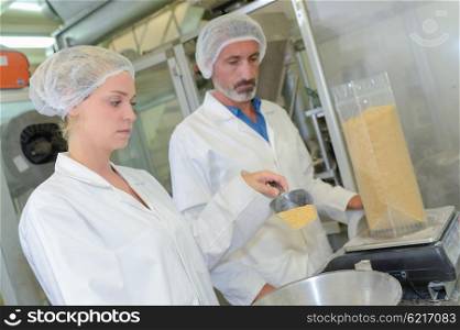 Male and female factory workers weighing ingredients