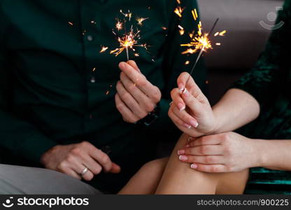Male and female hands hold lit Bengal lights. Beautiful happy young family celebrating Christmas together. Couple holding bengal light.. Couple holding bengal light. Male and female hands hold lit Bengal lights. Beautiful happy young family celebrating Christmas together.