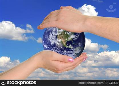 male and female hands holding the earth on background the sky
