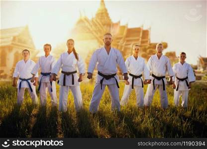 Male and female karate group in kimono against ancient temple on sunset. Martial art training outdoor. Photo manipulation with background. Male and female karate group against temple