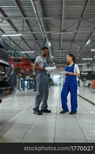 Male and female mechanics inspects engine, car service. Vehicle repairing garage, men in uniform, automobile station interior on background. Professional auto diagnostics. Male and female mechanics, car service