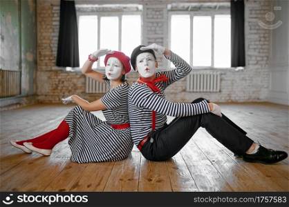 Male and female mime artists sitting on the floor, love couple parody scene, comedy. Pantomime theater, comedian, positive emotion, humour performance, funny face mimic and grimace. Male and female mime artists sitting on the floor