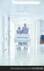 Male and female nurses pushing patient bed on hospital corridor