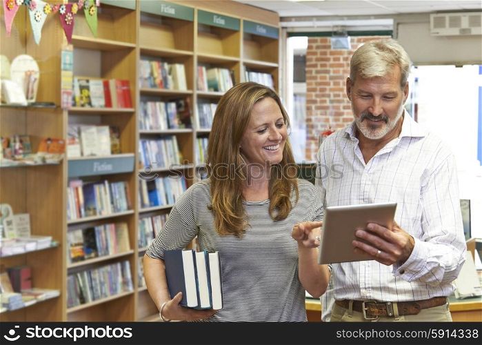 Male And Female Owners Of Bookstore Using Digital Tablet