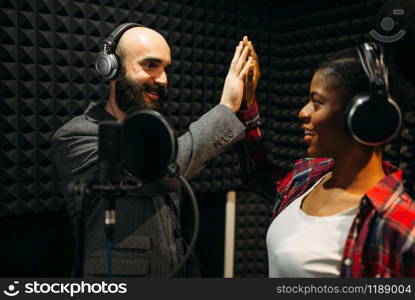 Male and female performers in headphones songs in audio recording studio. Musicians on record, professional music mixing