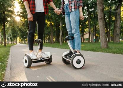 Male and female person riding on gyro board in park at sunset. Outdoor recreation with electric gyroboard. Transport with balance technology, gyroscope. Male and female person on gyro board at sunset