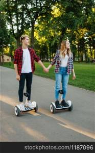 Male and female person riding on gyro board in park. Outdoor recreation with electric gyroboard. Transport with balance technology. Male and female person riding on gyroboard in park