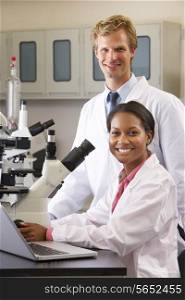 Male And Female Scientists Using Microscopes In Laboratory