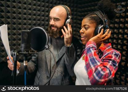 Male and female singers in headphones songs in audio recording studio. Musicians on record, professional music mixing