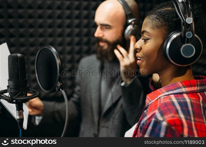 Male and female singers in headphones songs in audio recording studio. Musicians on record, professional music mixing. Male and female singers in audio recording studio