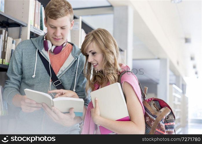 Male and female students discussing over books by shelf at university library