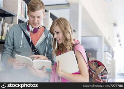 Male and female students discussing over books by shelf at university library