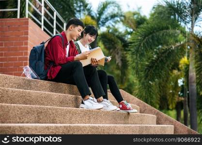 Male and female students sitting and reading books on the stairs.