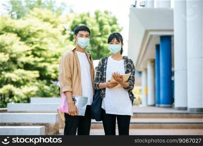 Male and female students wear a health mask and talk to each other on the stairs.