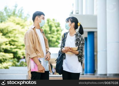Male and female students wear a health mask and talk to each other on the stairs.