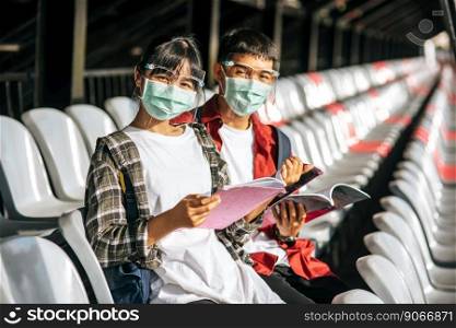 Male and female students wear masks and sit and read on the field chair.