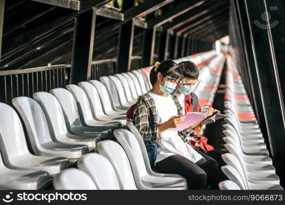 Male and female students wear masks and sit and read on the field chair.