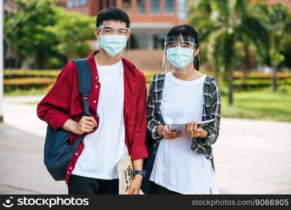Male and female students wear masks and stand in front of the university.