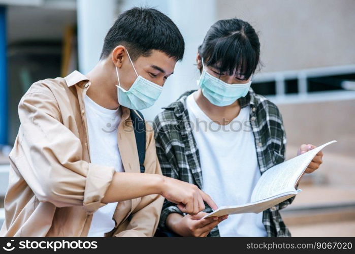 Male and female students wearing masks sit and read books on the stairs