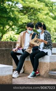 Male and female students wearing masks sit and read books on the stairs